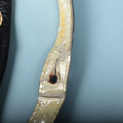 Close-up of tears and cracking in the pearloid around a secondary strap button hole.