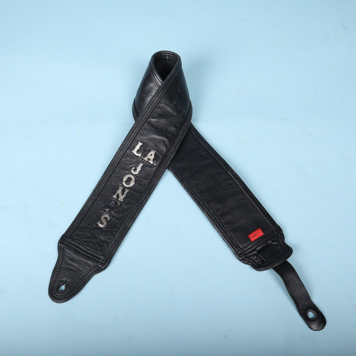 Another folded view of the black Action bass guitar strap against a light blue background.