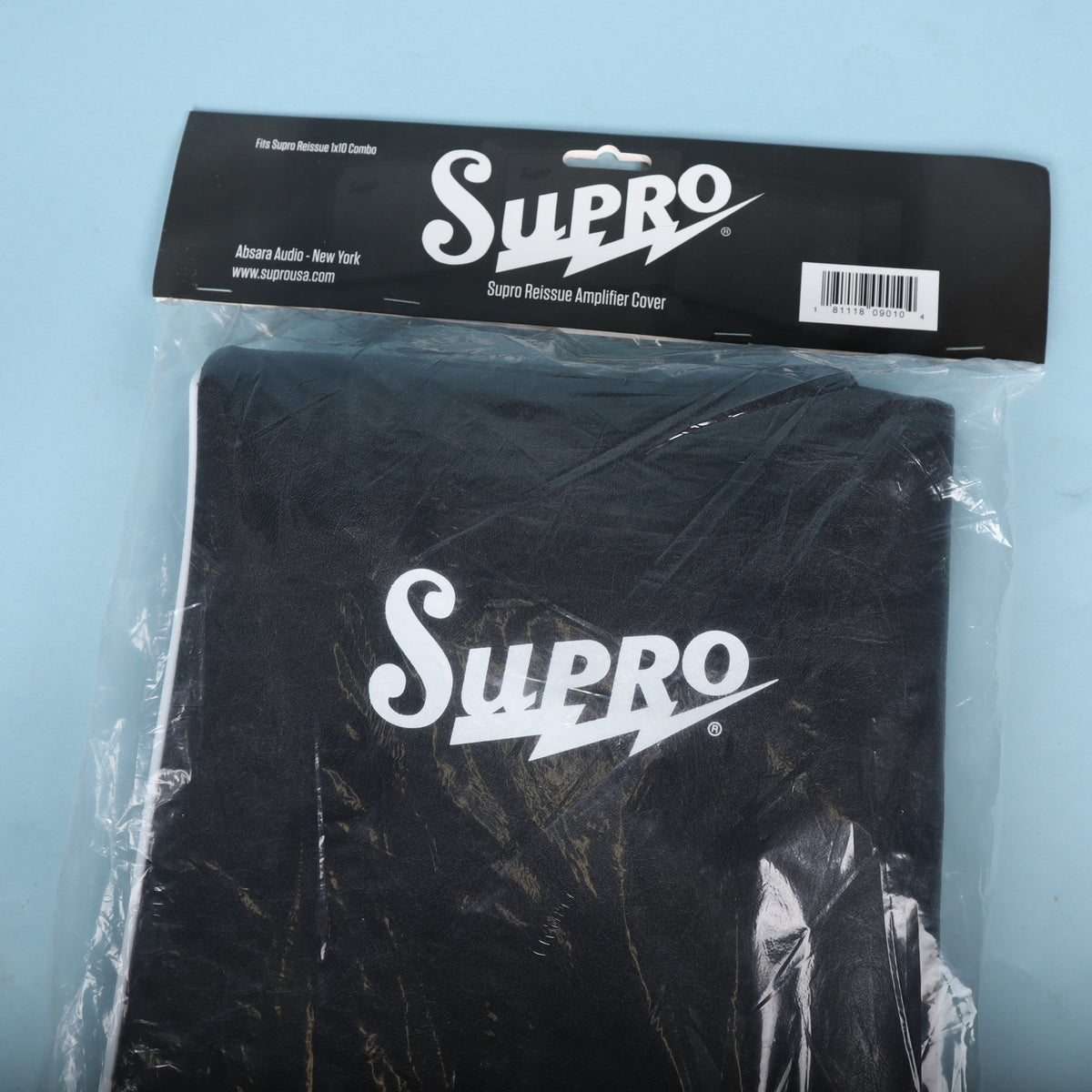 Close-up front view showing white Supro logo on black amplifier cover inside packaging.