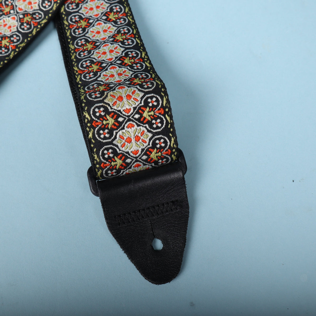 Close-up of the leather end tab and woven floral pattern of the Ernie Ball jacquard guitar strap