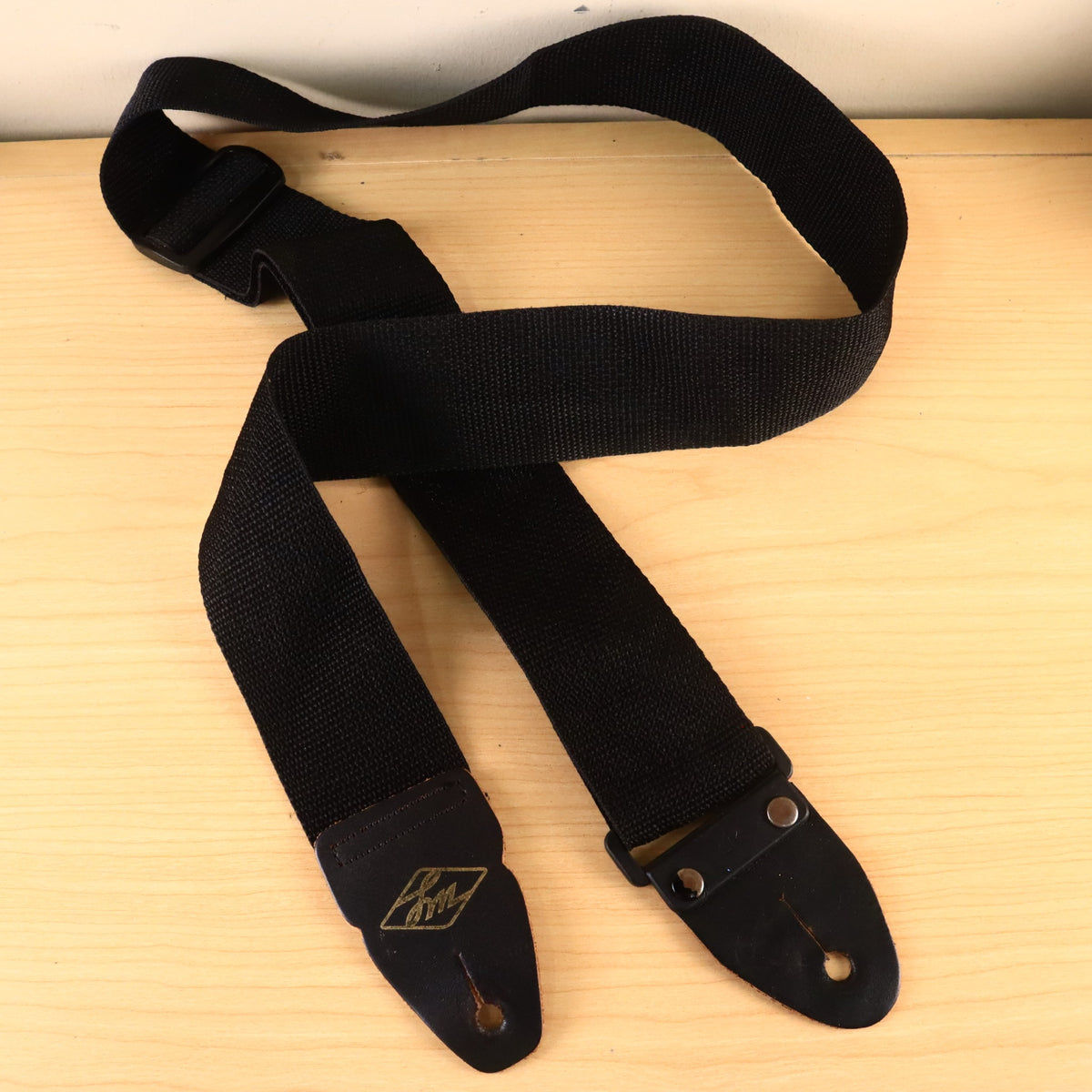 Full view of a black LM woven nylon guitar strap with leather end tabs laid out on a wooden surface.