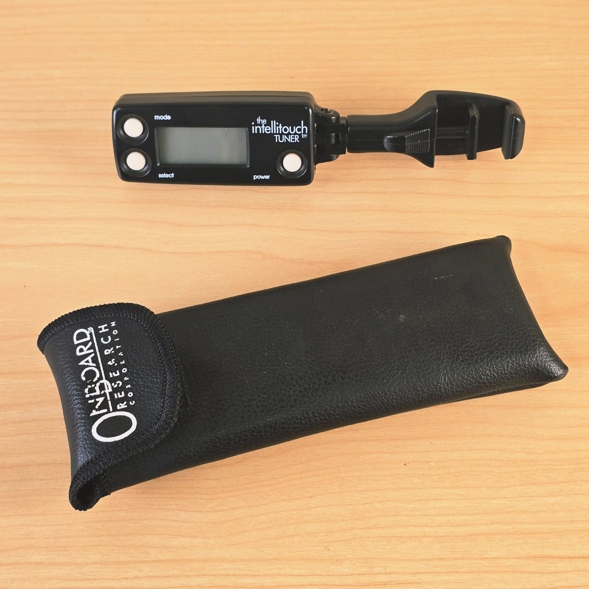 Top-down view of The Intellitouch Tuner and carrying pouch on a wooden surface.