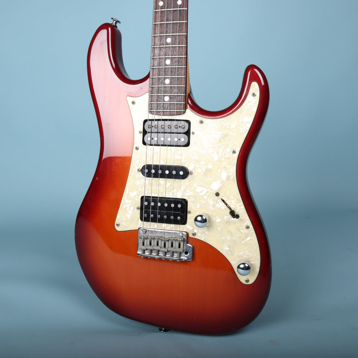 Close-up view of red sunburst body, HSH pickup configuration, bridge, and controls.