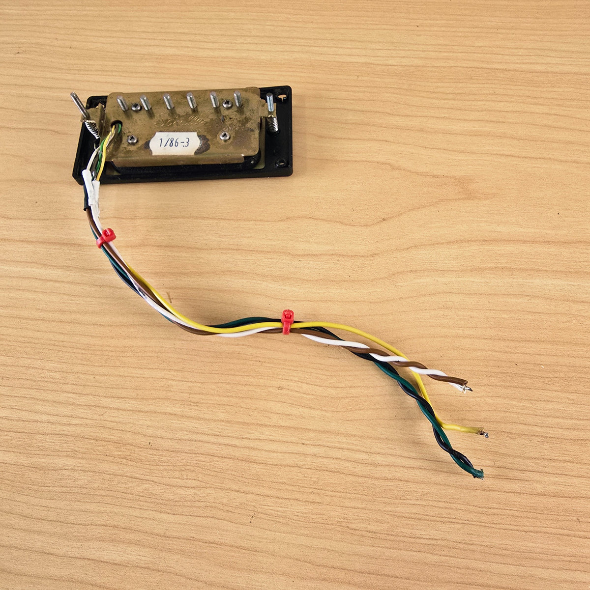 Underside of Schaller humbucker displaying brass plate, height screws, and multi-color lead wire