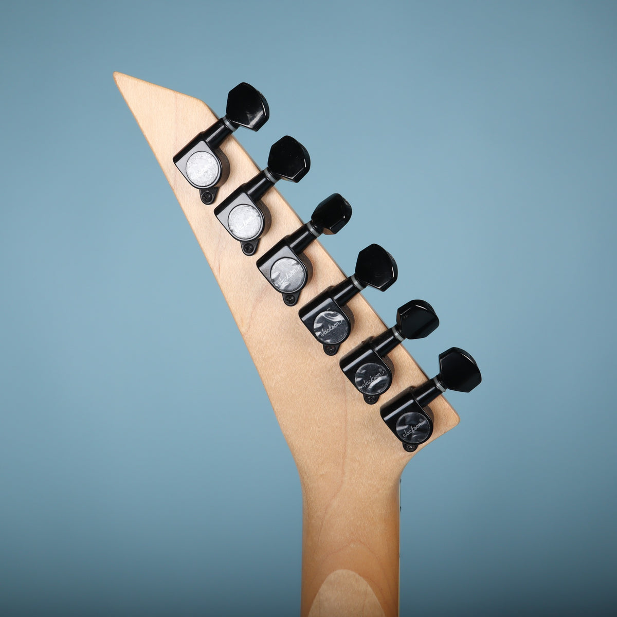 Rear view of pointed headstock with six inline black Jackson tuning machines