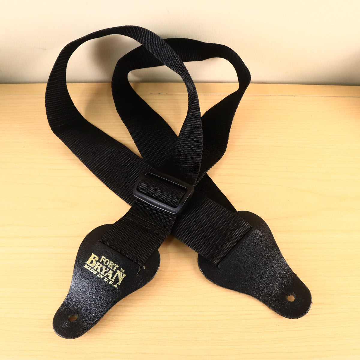 Full front view of black Fort Bryan webbing guitar strap with gold logo stamped on leather end.