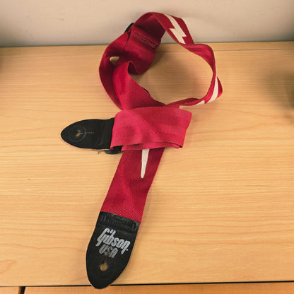 Angled view of the red Gibson guitar strap showing the adjustable buckle and end tab