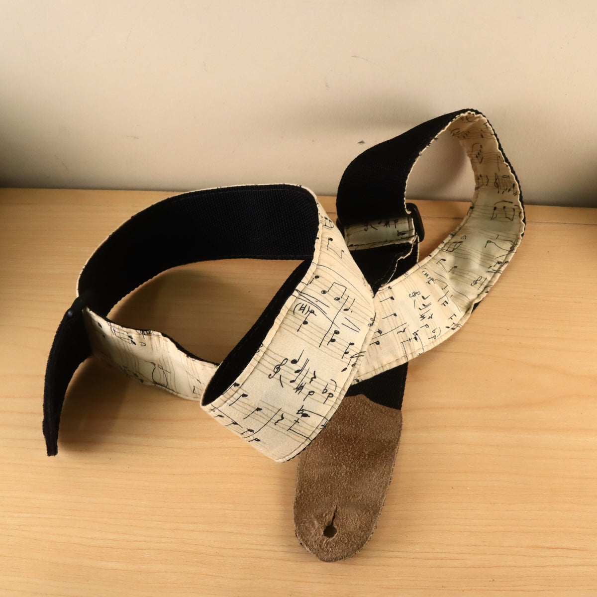 Guitar strap displaying black woven backing and tan suede underside on one end tab.