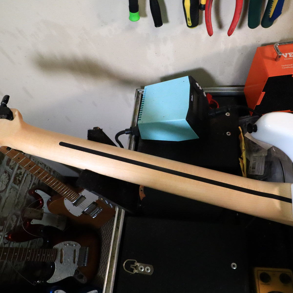 Bottom edge view of guitar body resting on padded tech workbench.