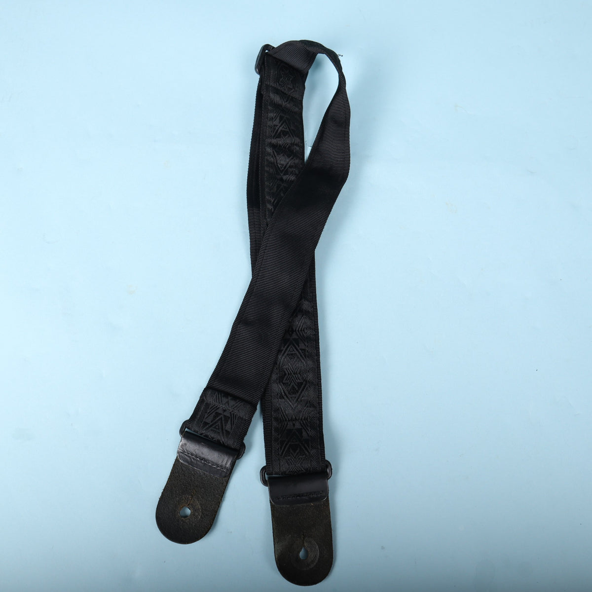 Underside of the Planet Waves woven guitar strap showing black backing webbing and leather tabs.