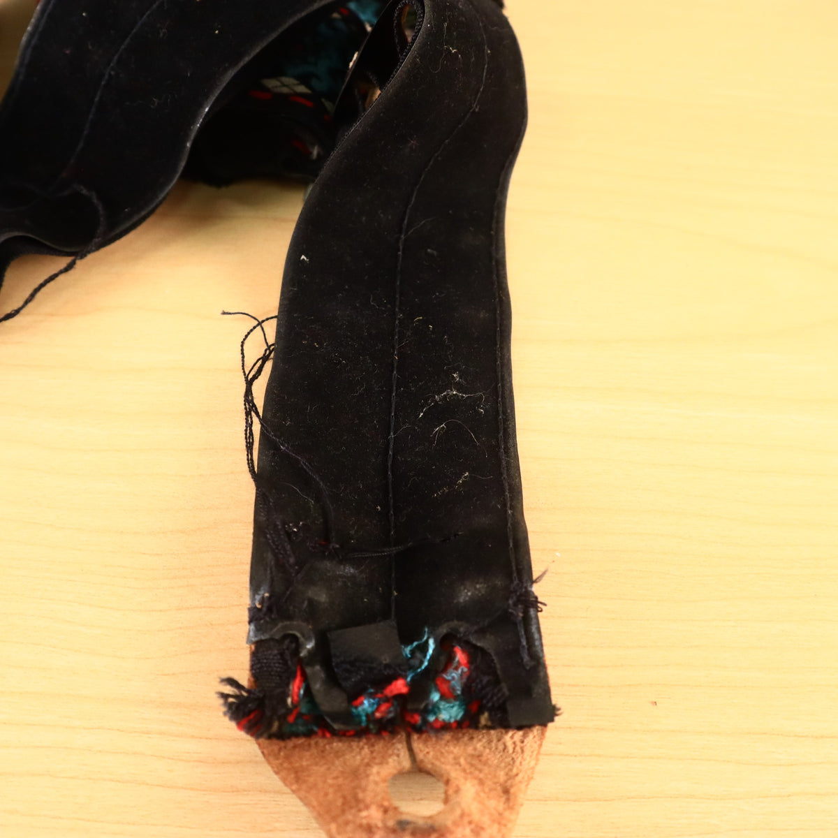 Frayed edge and black backing near leather end tab of woven guitar strap.