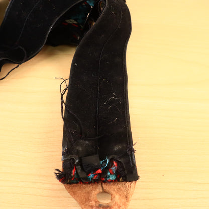 Frayed edge and black backing near leather end tab of woven guitar strap.