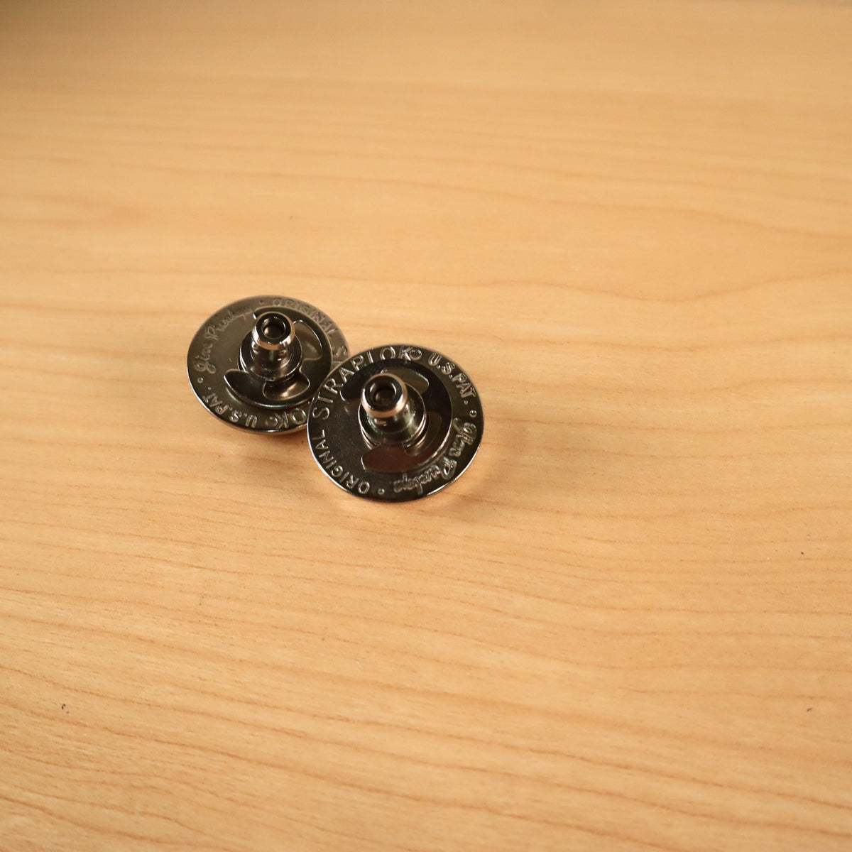 Two Jim Dunlop Original Straplok quick-release strap attachments, showing the engraved top buttons on a wooden surface.