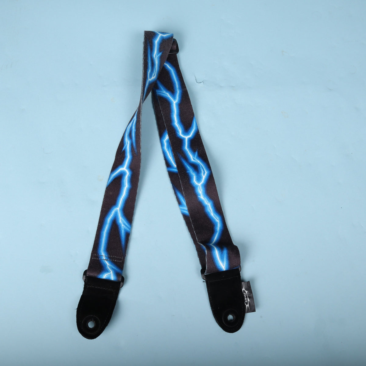 Perri's blue lightning bolt guitar strap folded on a blue surface