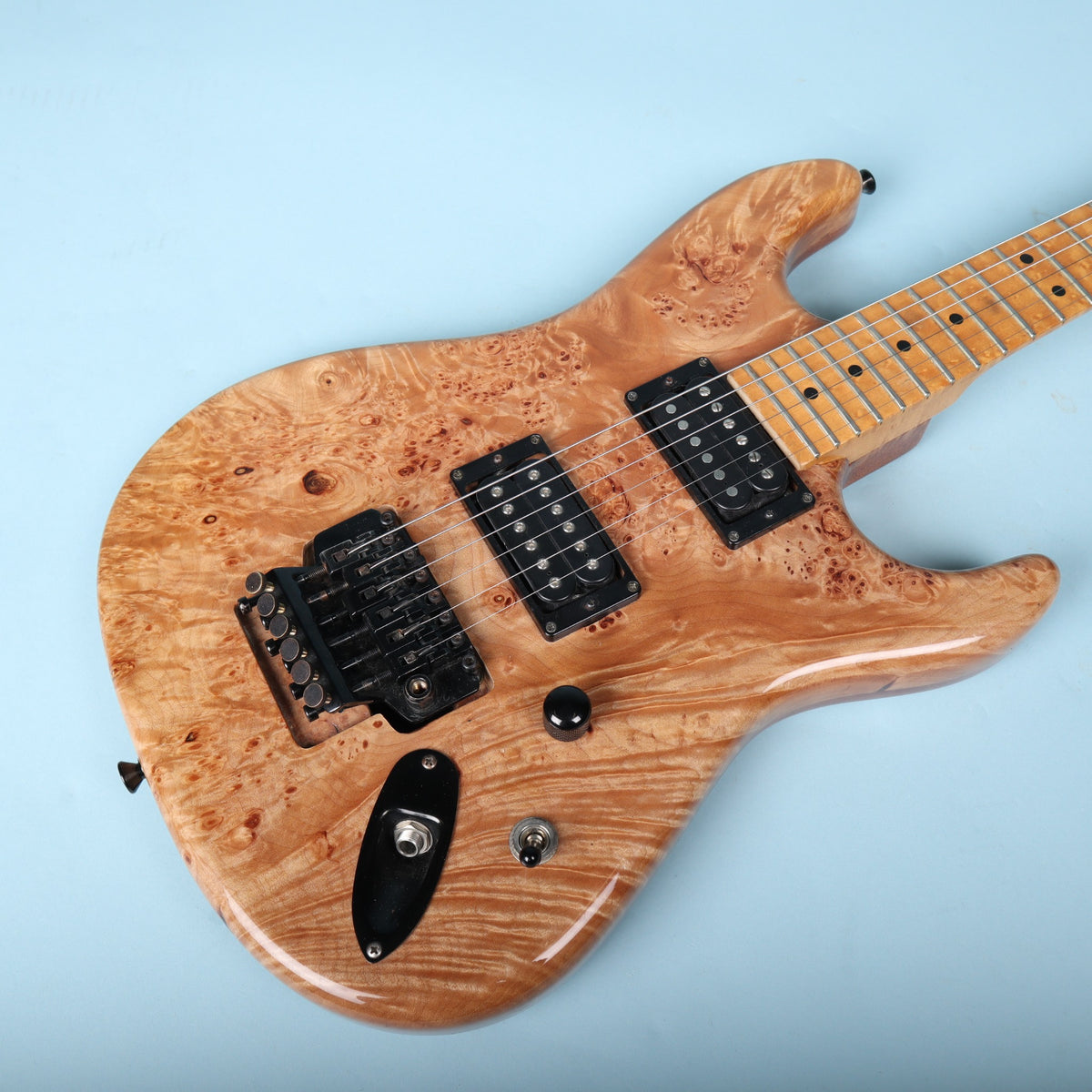 Angled front view of burl maple guitar body resting on studio backdrop.