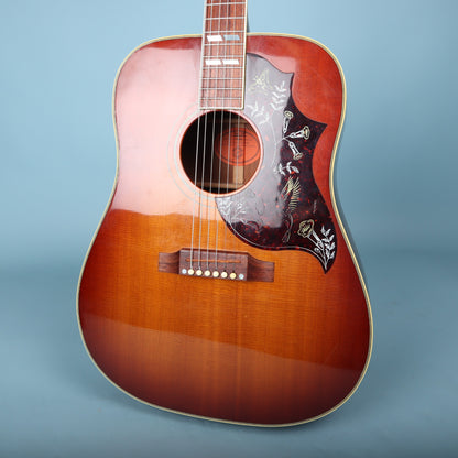Close-up view of the sunburst body and pickguard of the Gibson Hummingbird against a blue background.