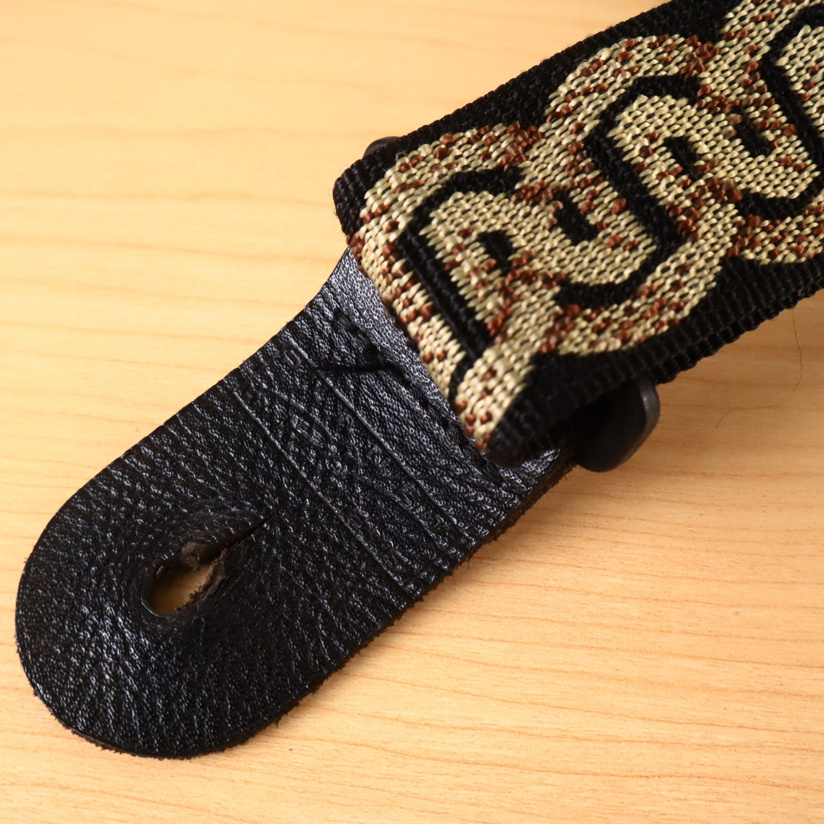 Detailed view of the textured black leather end tab on the Planet Waves strap.
