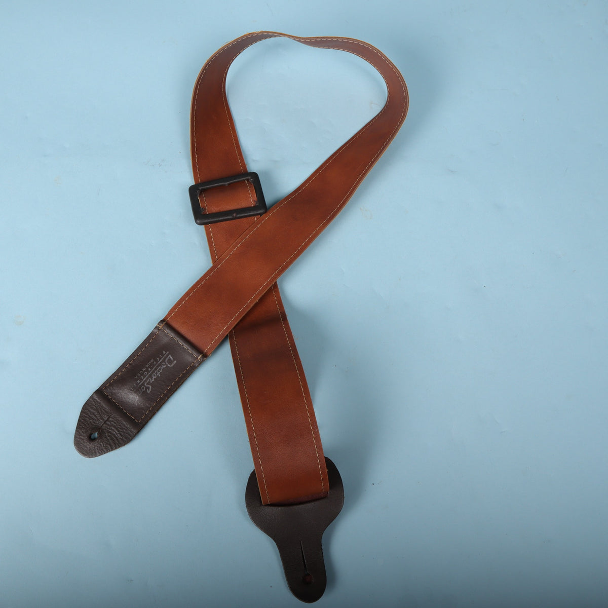 Doctor Song Pick-Pocket leather guitar strap laid out in a loop against a light blue background.