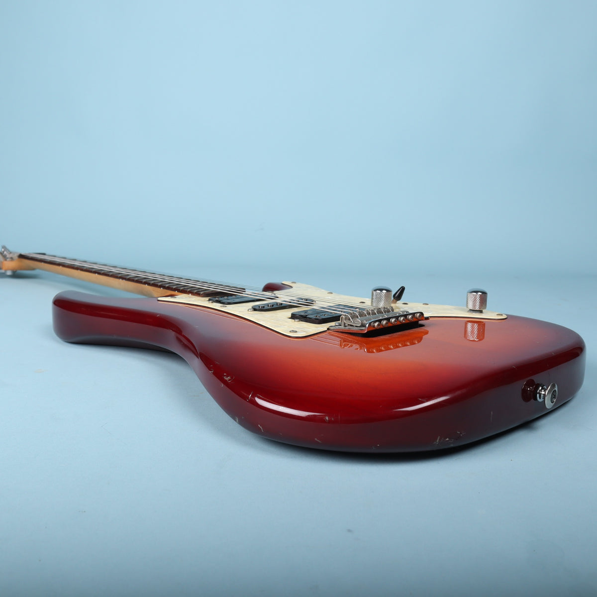 Side perspective of guitar body resting horizontally on studio background.