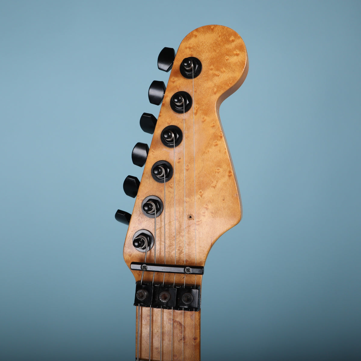 Front view of natural birdseye maple headstock with black hardware.