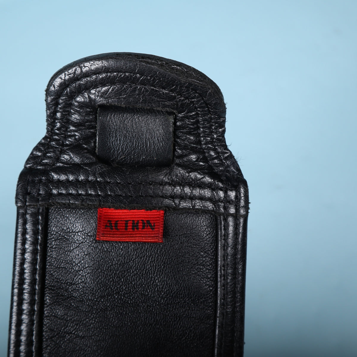 Close-up of the red Action brand fabric label sewn onto the black leather end of the strap.