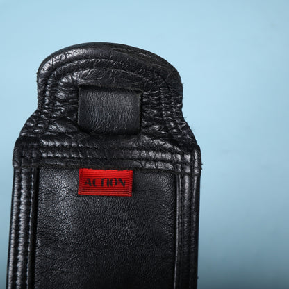 Close-up of the red Action brand fabric label sewn onto the black leather end of the strap.