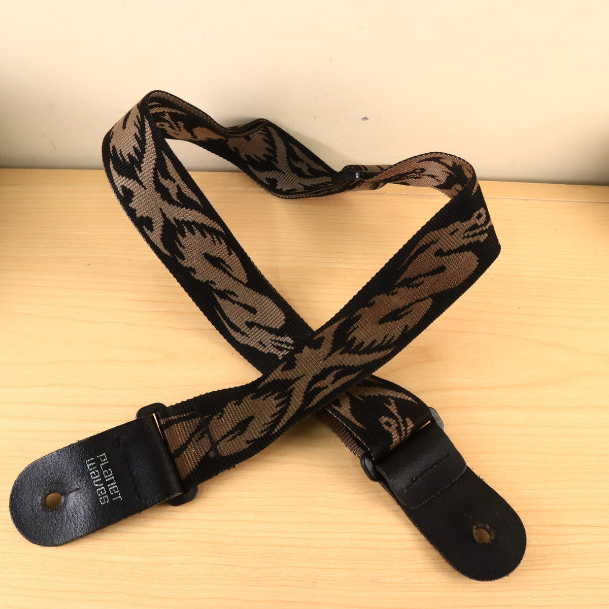 Planet Waves woven guitar strap crossed over itself on a light wood tabletop.