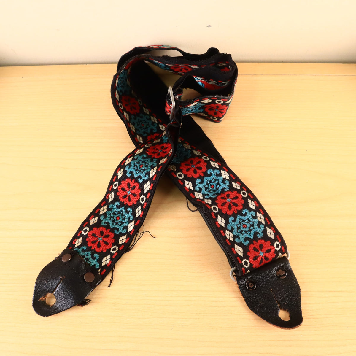 Full view of woven bohemian guitar strap laid out on wood surface.