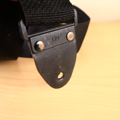 Close-up of black leather strap end with metal rivets and plastic connector stamped LM.
