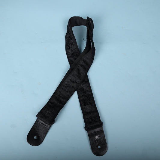 Full view of the Planet Waves black jacquard woven guitar strap against a blue backdrop.