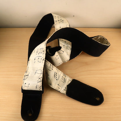 Sheet music printed fabric guitar strap laid out with plastic tri-glide adjustment buckle visible.