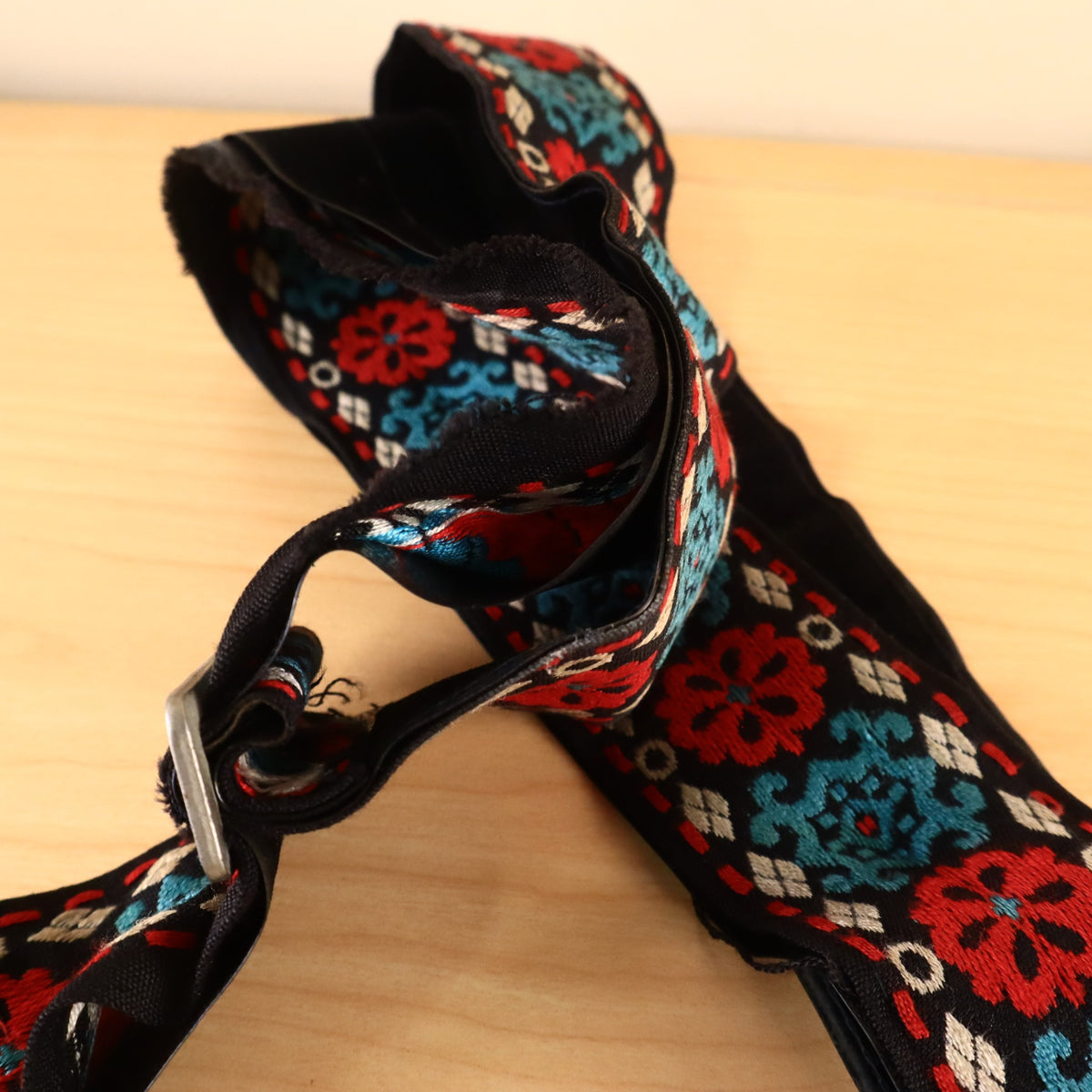 Detail view of metal slide buckle on red and teal woven pattern strap.