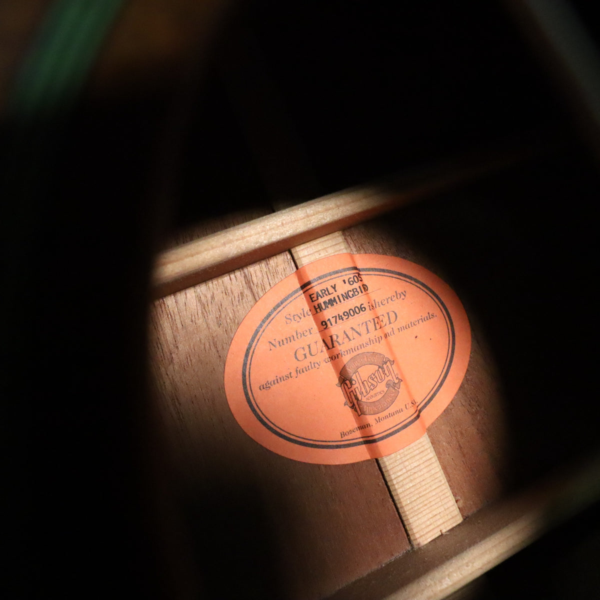 Interior view of the soundhole showing the orange oval label printed with 'EARLY '60S Style HUMMINGBIRD' and serial number 91749006.