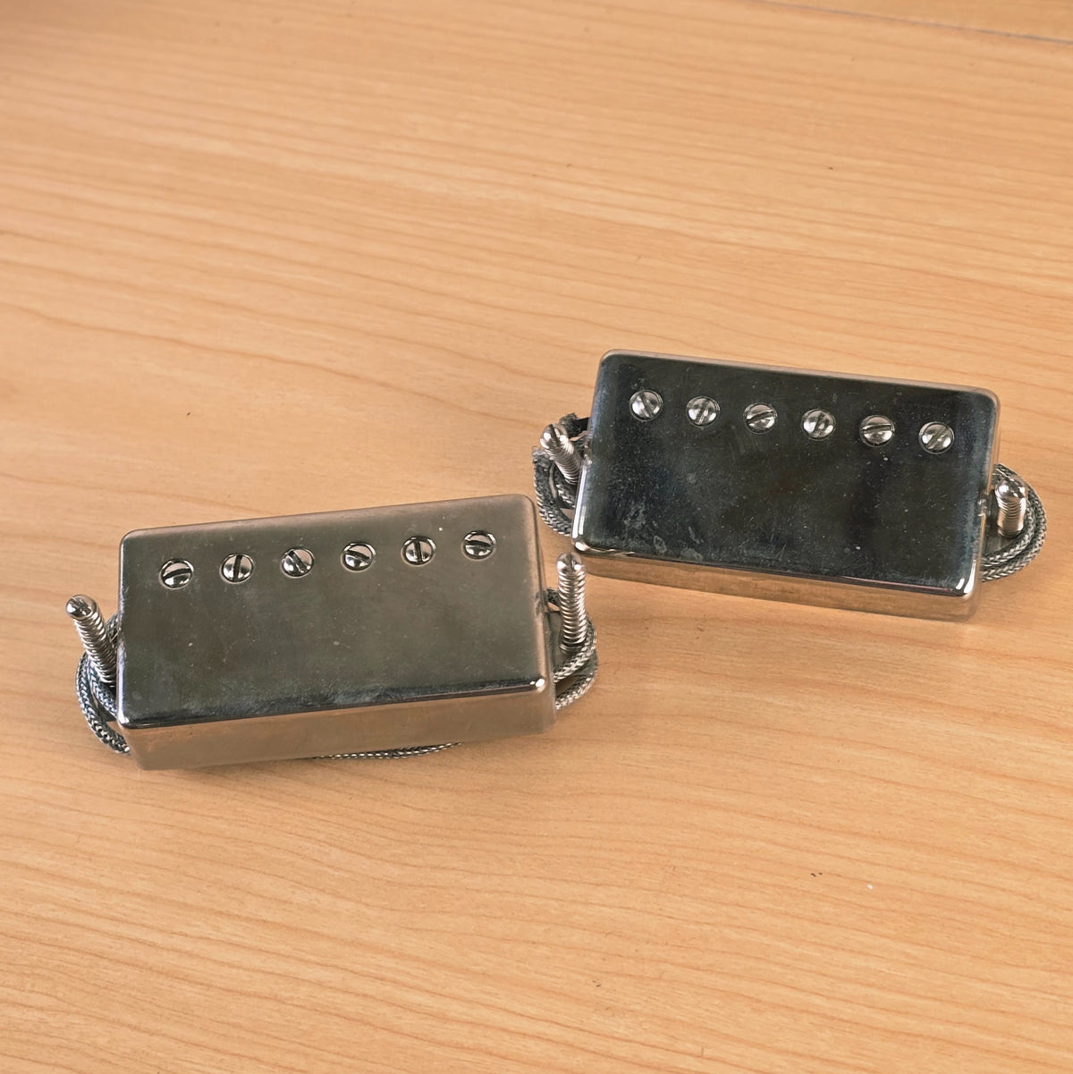 Angle view of two nickel Lollar Imperial humbucker pickups on a wooden surface.