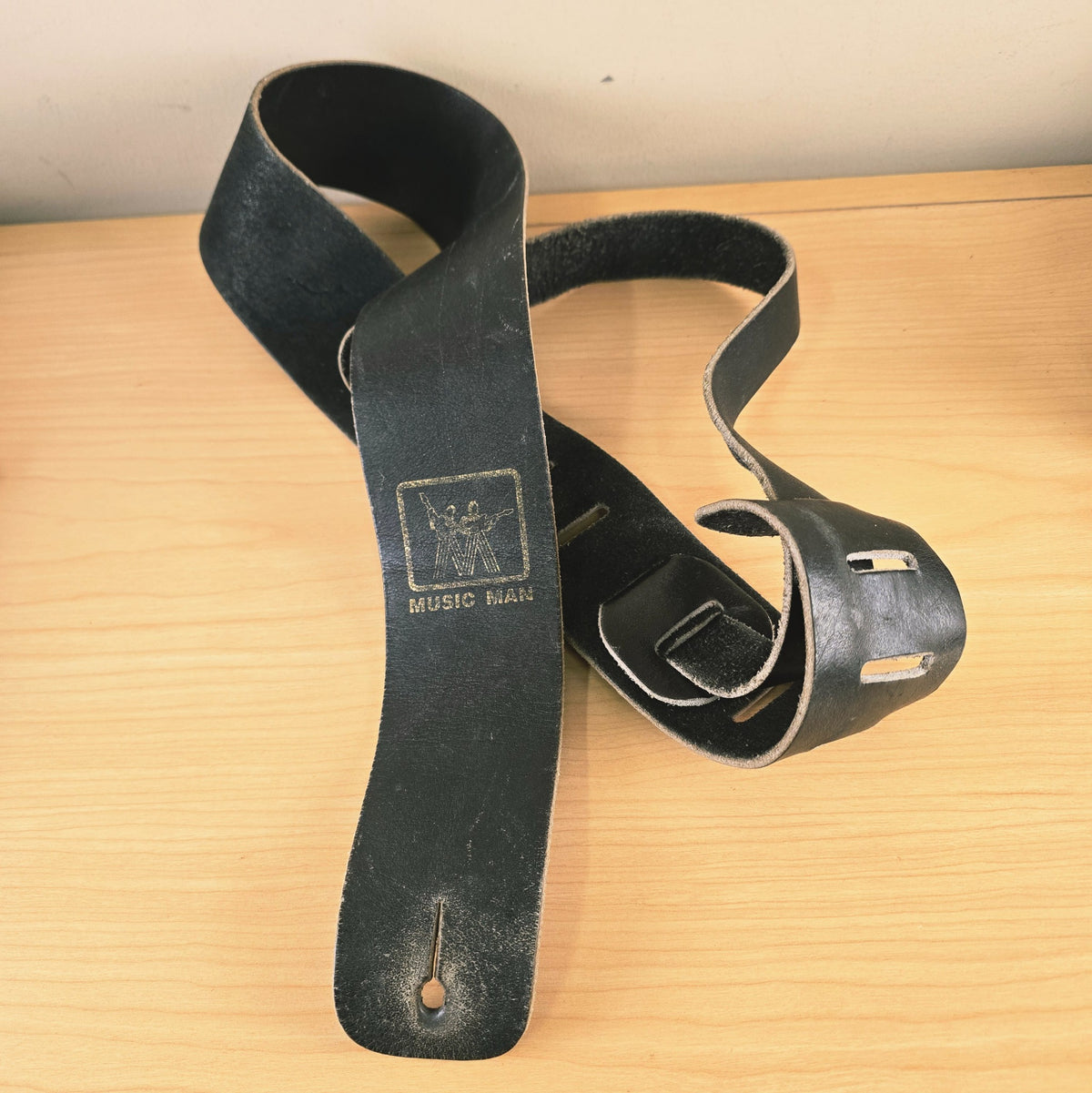Full view of vintage Music Man black leather guitar strap showing stamped logo