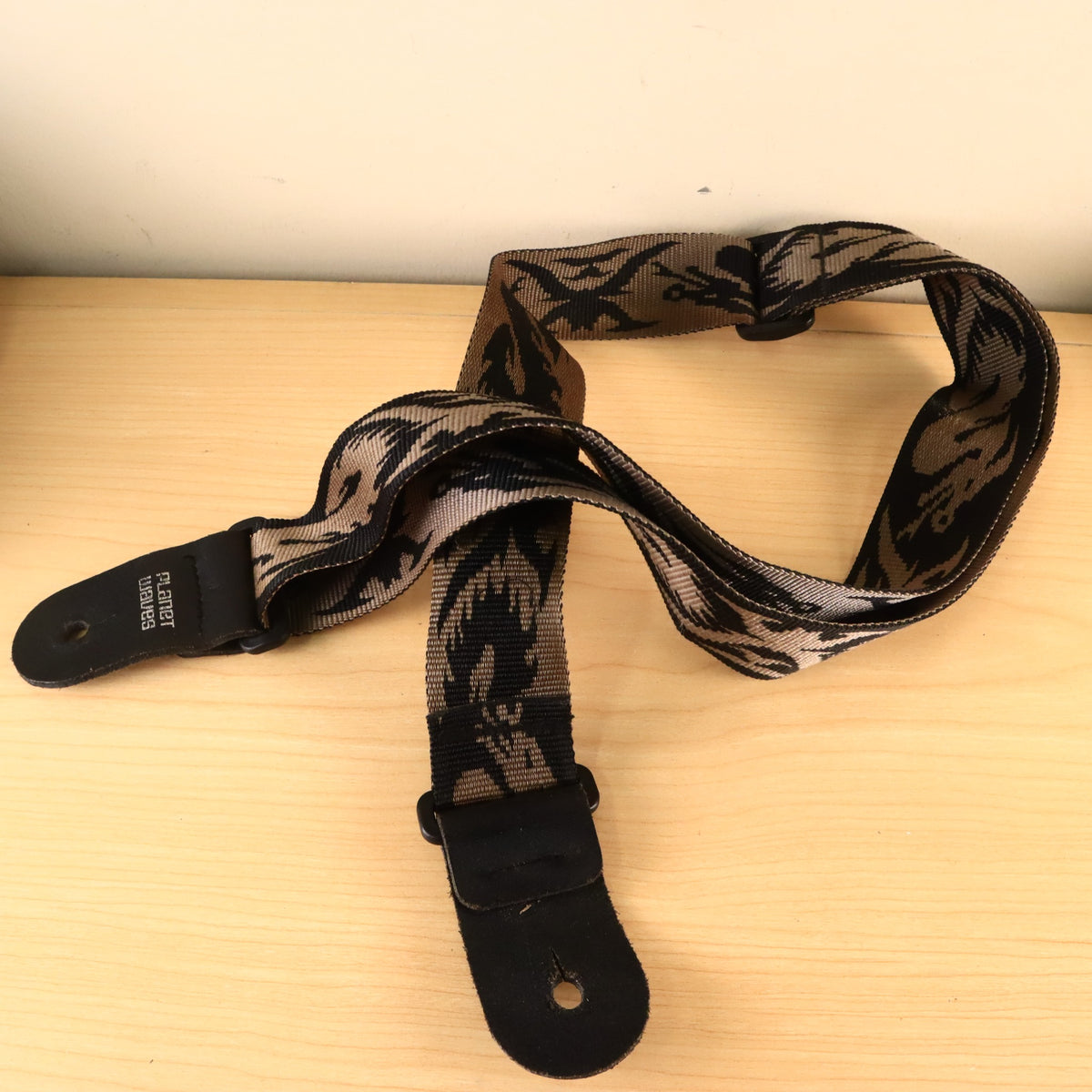 Planet Waves woven pattern guitar strap displayed on a wooden surface showing leather end tabs.