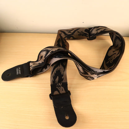 Planet Waves woven pattern guitar strap displayed on a wooden surface showing leather end tabs.
