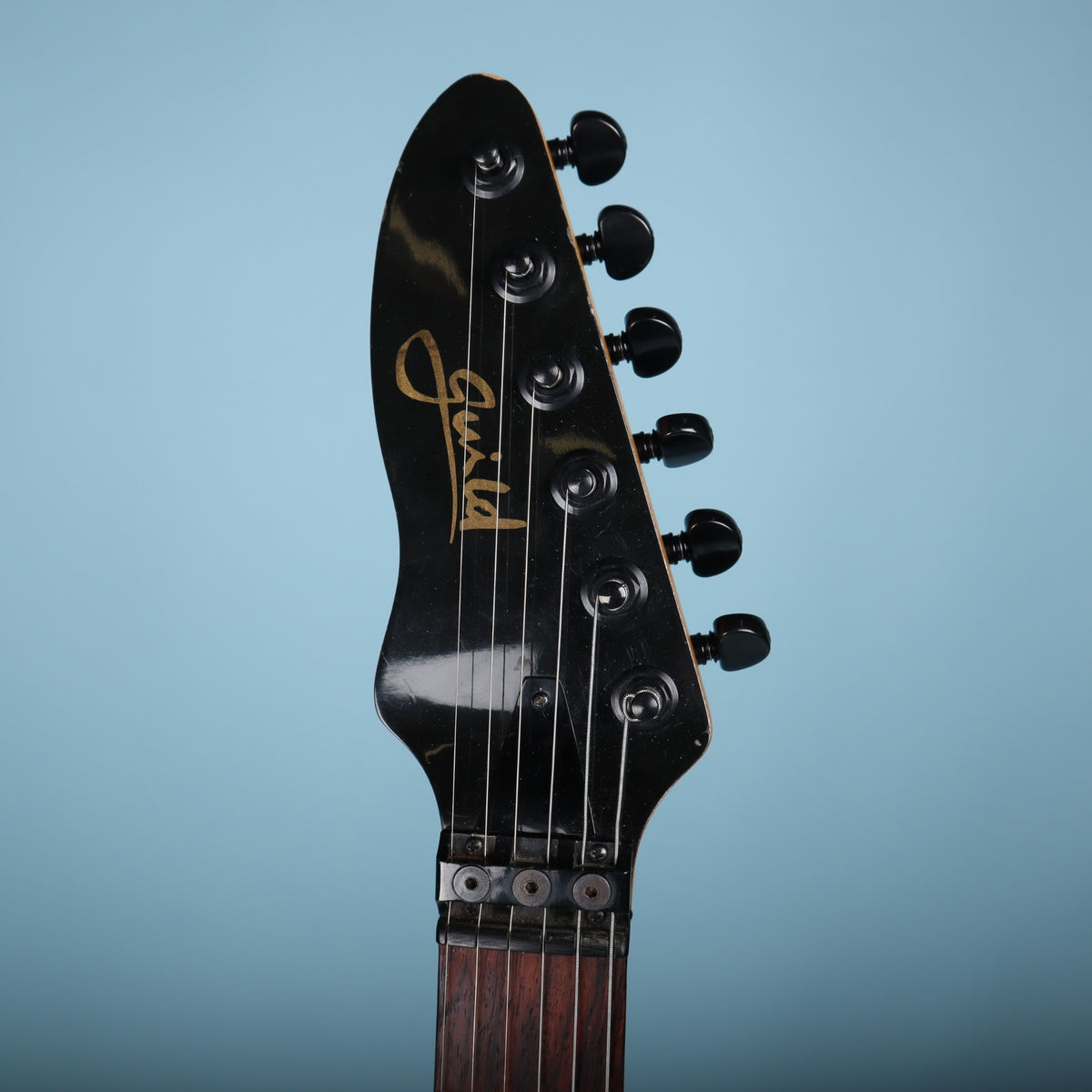 Headstock face displaying the gold Guild logo, black hardware, and string lock