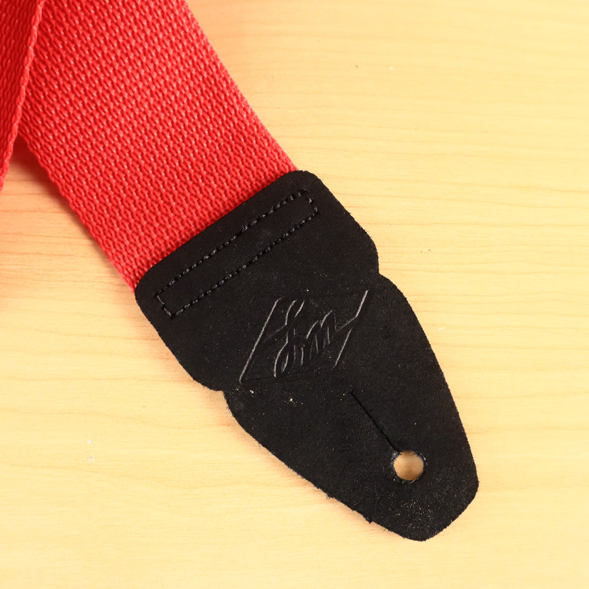 Close-up of black leather end tab with embossed LM logo stitched to red webbing.