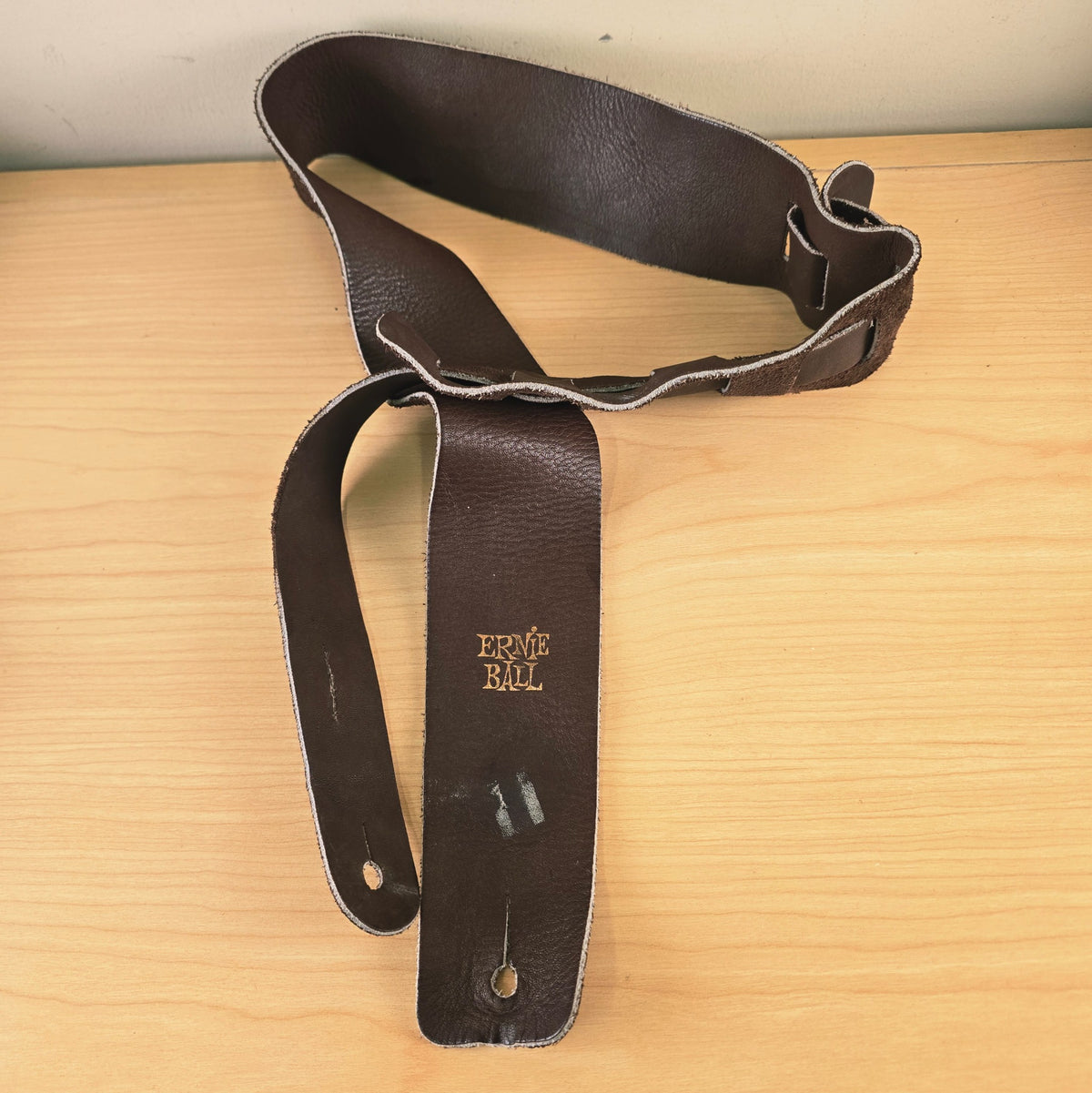 Ernie Ball 2.5-inch brown leather guitar strap coiled on a wooden surface