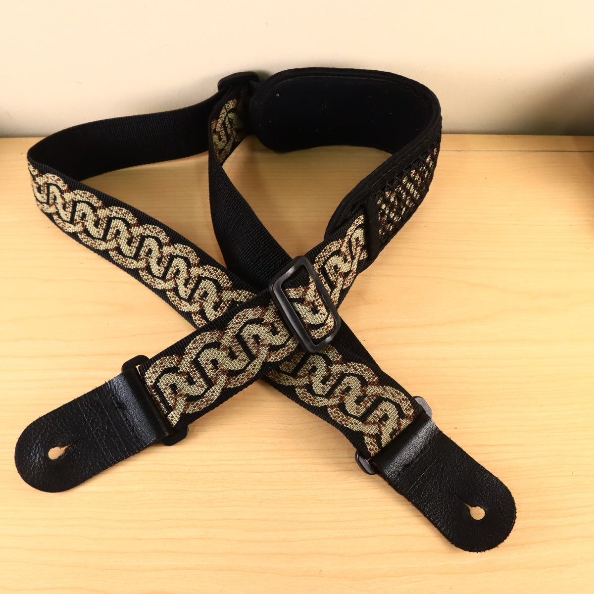 Planet Waves Celtic pattern guitar strap configured in an overlapping loop showing the adjustment buckle.