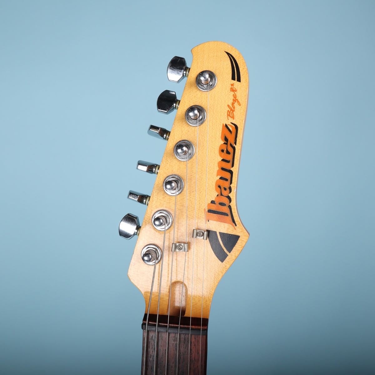 Front of headstock showing black and orange Ibanez Blazer logo and string trees.