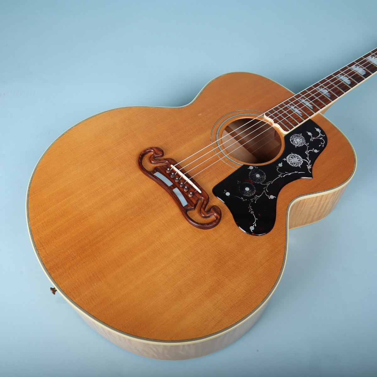Angled front view of guitar body highlighting natural finish top and floral pickguard.