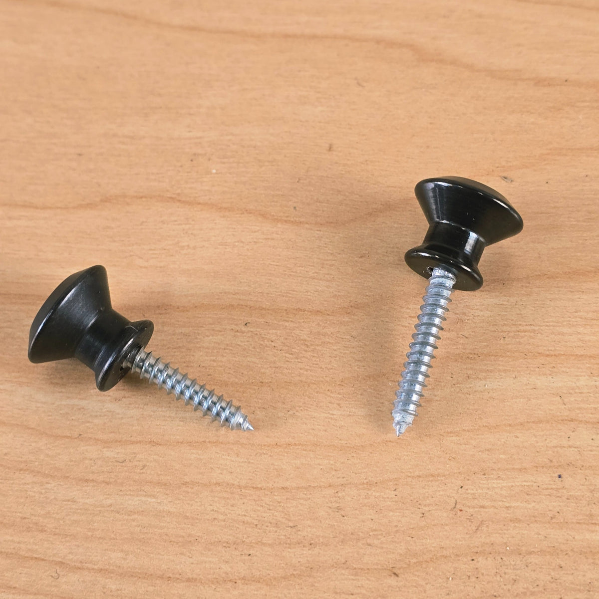 Pair of black Dunlop Straplok strap buttons laid out side by side on a wood surface