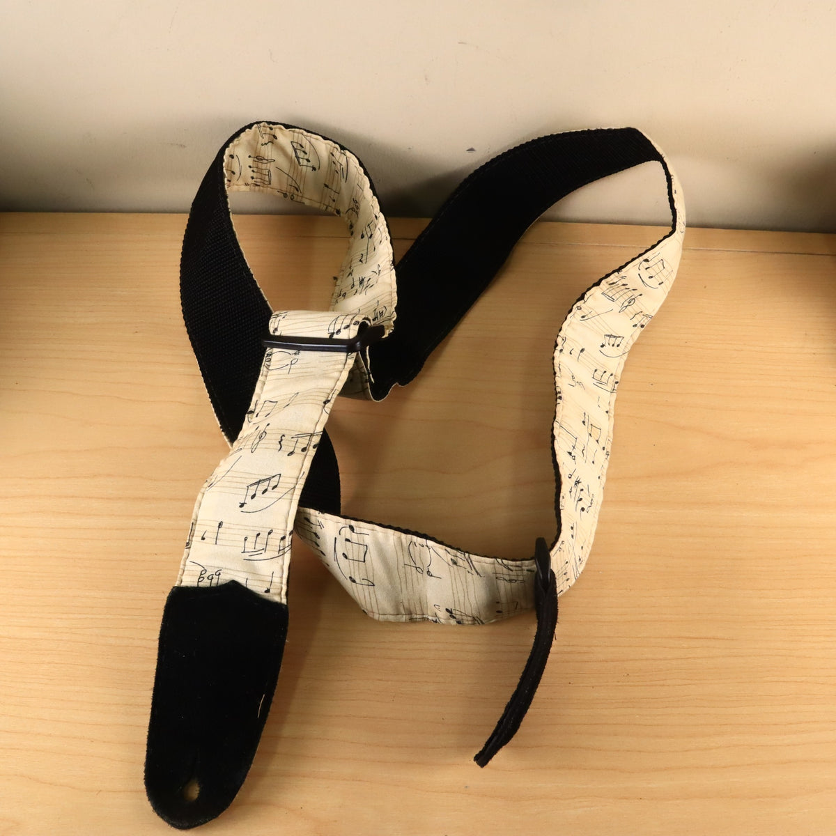 Coiled sheet music pattern guitar strap showing black suede end tab and plastic adjustment hardware.