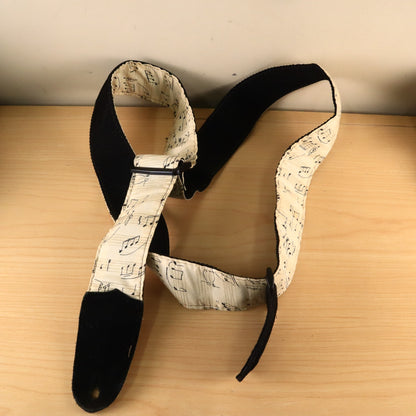 Coiled sheet music pattern guitar strap showing black suede end tab and plastic adjustment hardware.