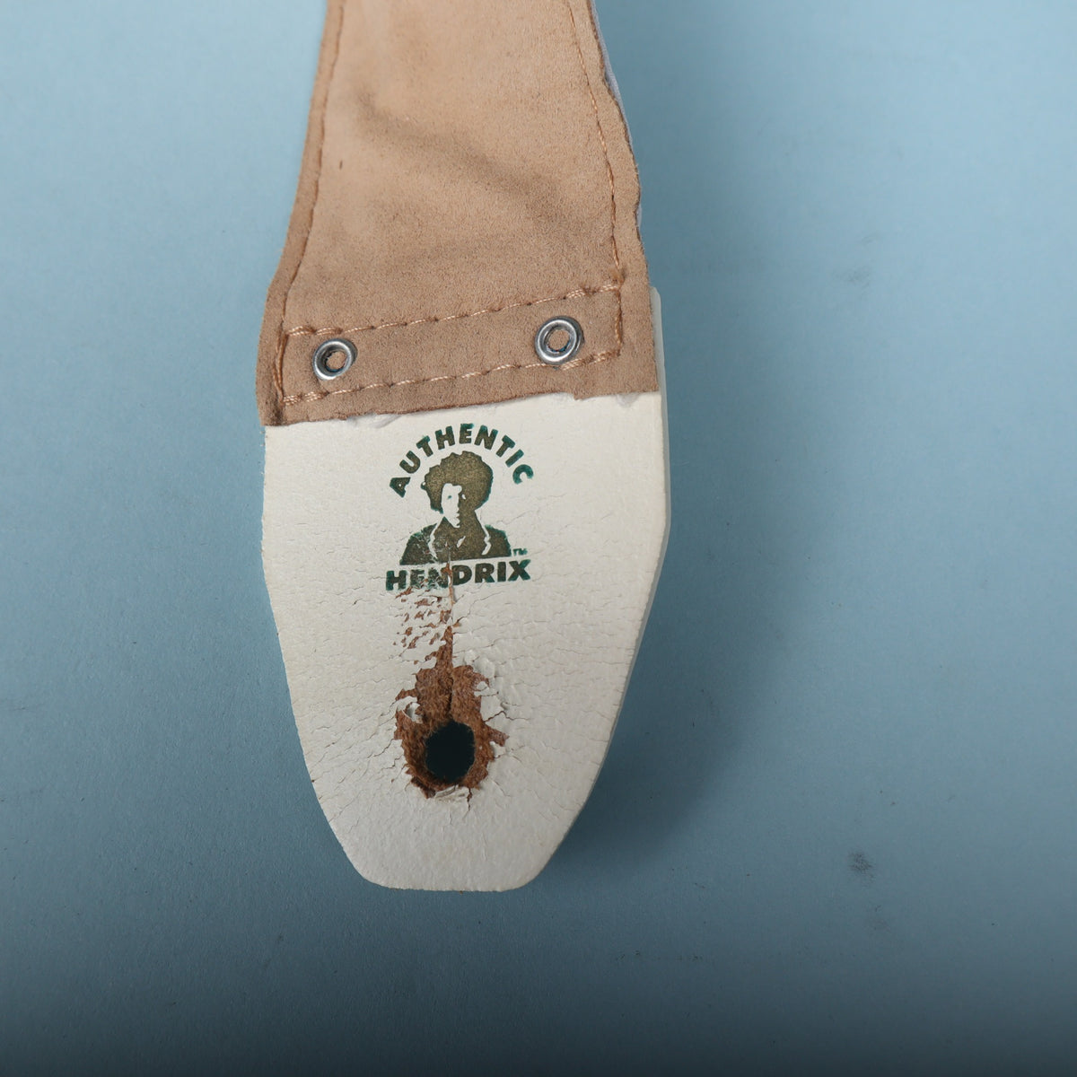 Close-up of the Authentic Hendrix logo on the white leather end tab showing surface peeling and wear around the pin hole