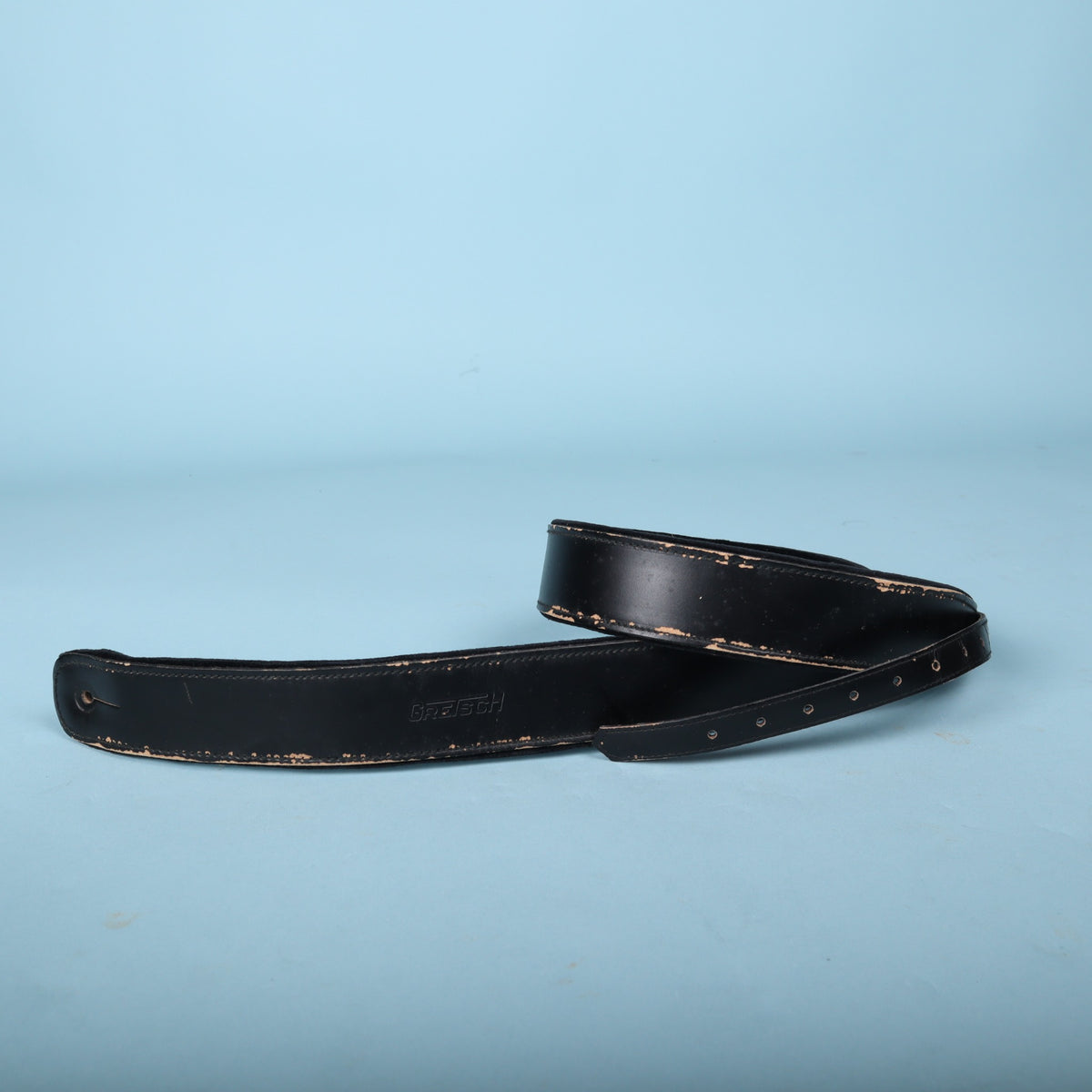 Gretsch black leather guitar strap coiled on a light blue background.