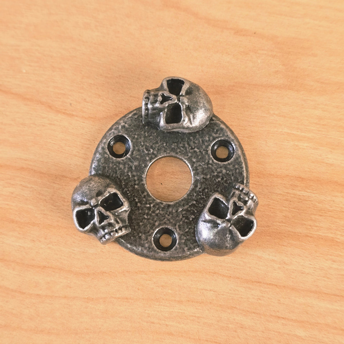 Overhead front view of the Gunther skull guitar switch or jack plate on a wood surface.