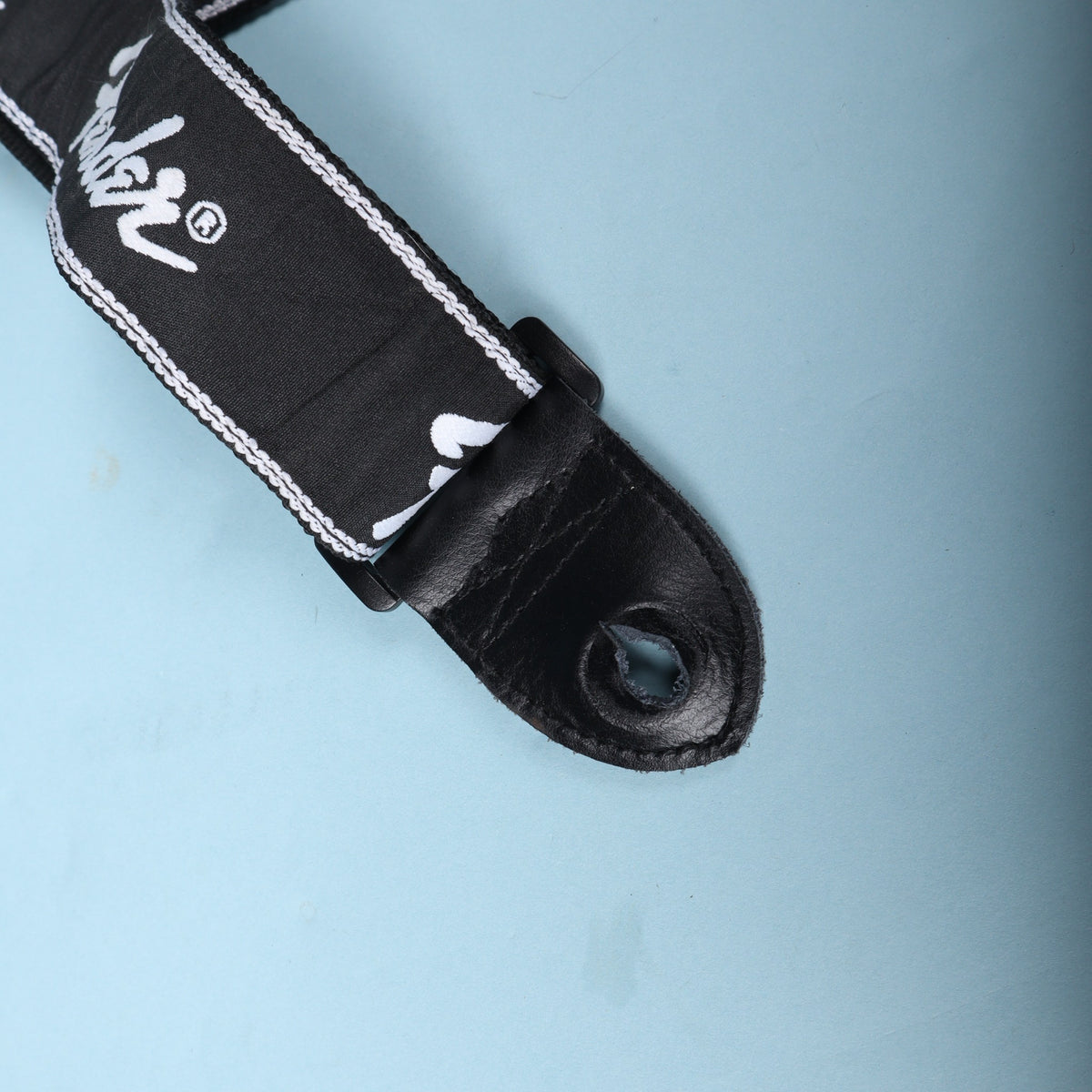 Detail of the buckle and leather end tab connection on a black Fender running logo strap
